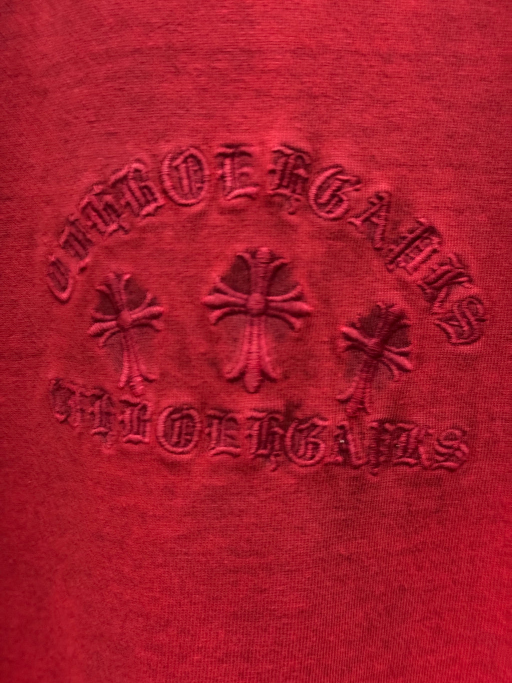 Red T-shirt fabric close-up showing embossed crest and decorative rhinestones