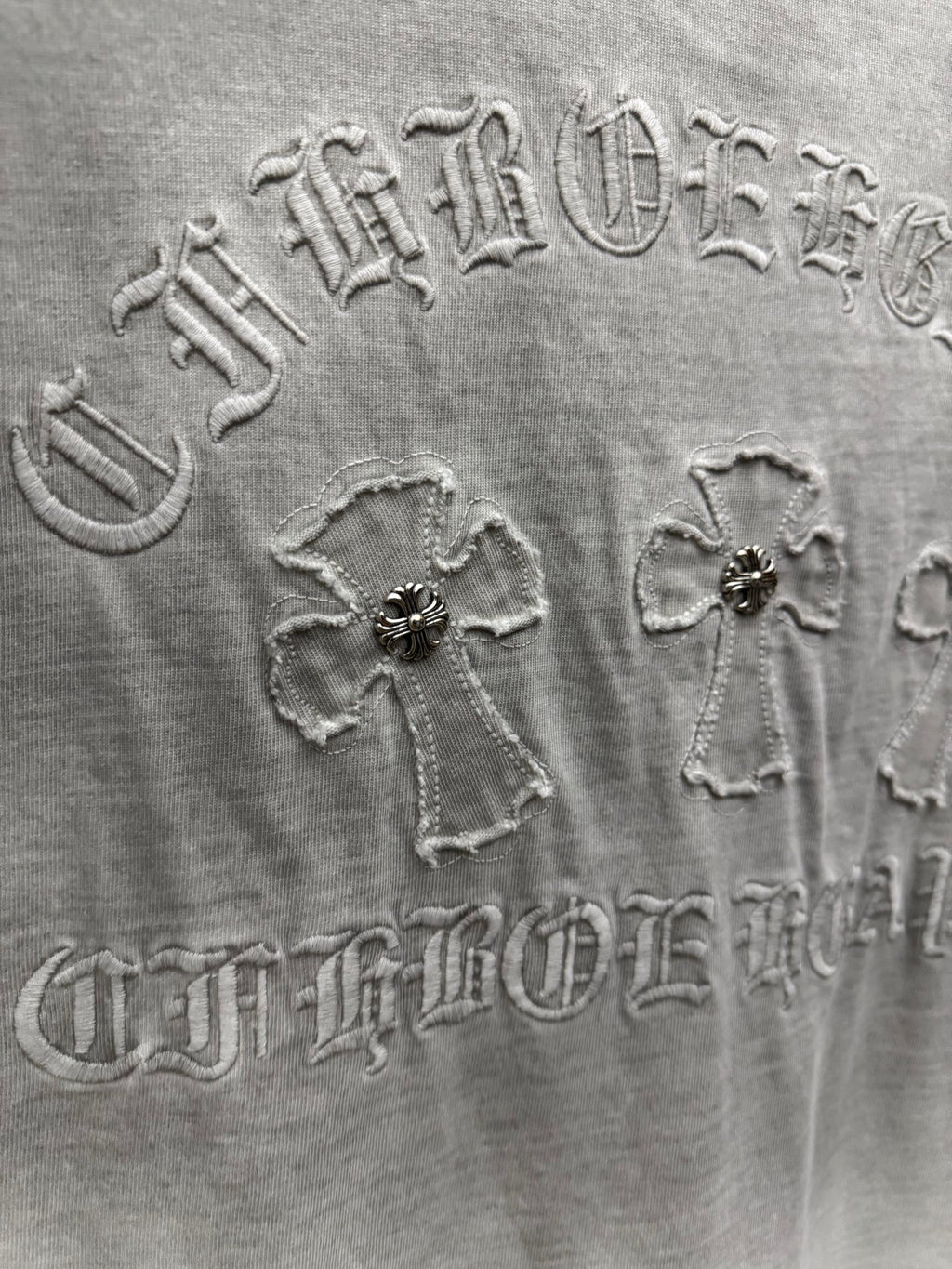 Light gray T-shirt back embroidery close-up with ornate lettering and cross motifs