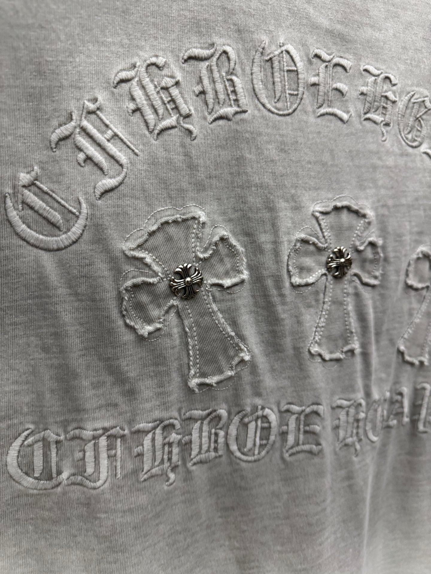 Light gray T-shirt back embroidery close-up with ornate lettering and cross motifs