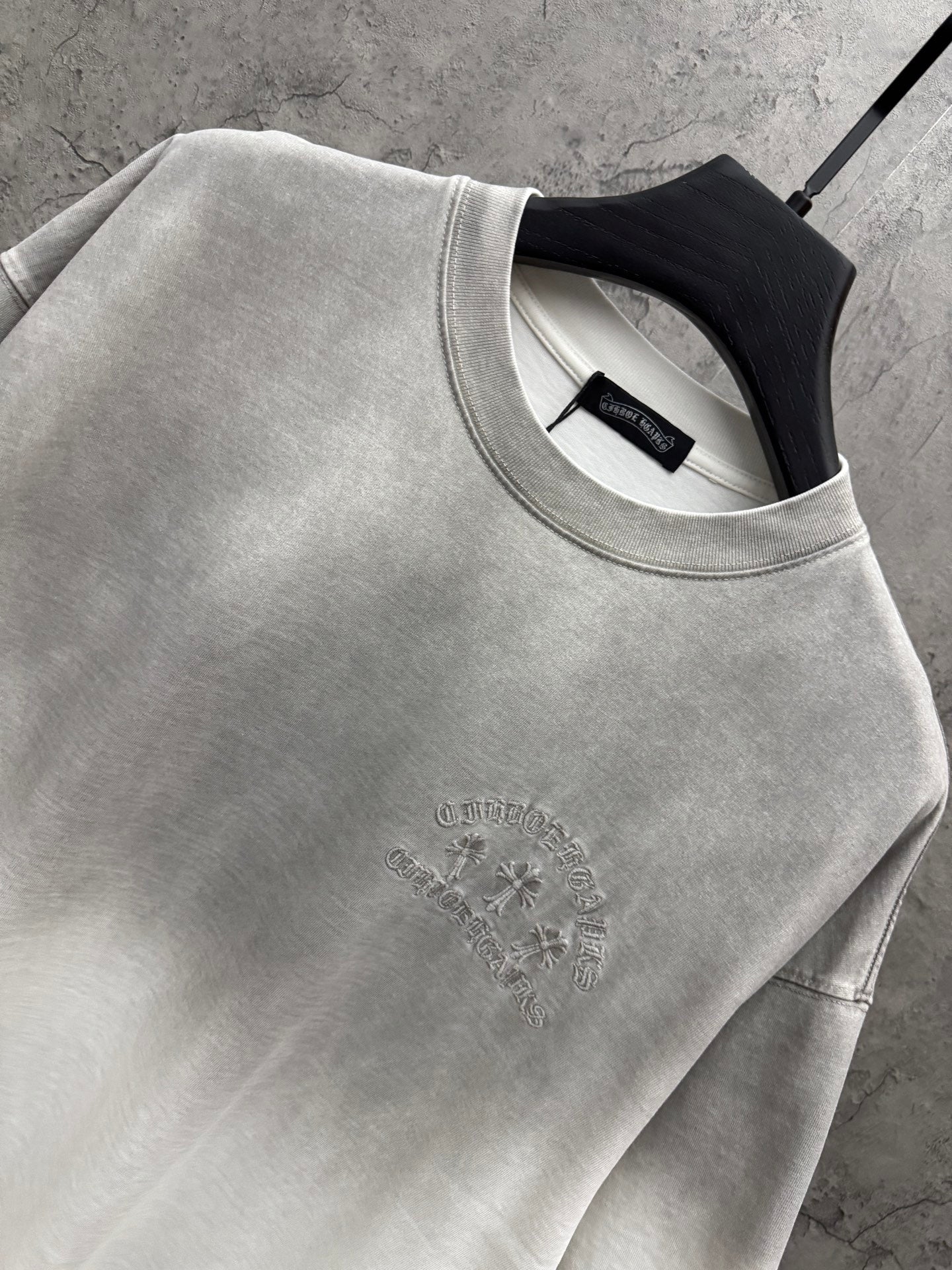 Light gray T-shirt close-up: crew neck and small centered chest embroidery detail