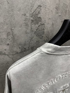 Light gray T-shirt back shoulder close-up with embroidered arched text near hem