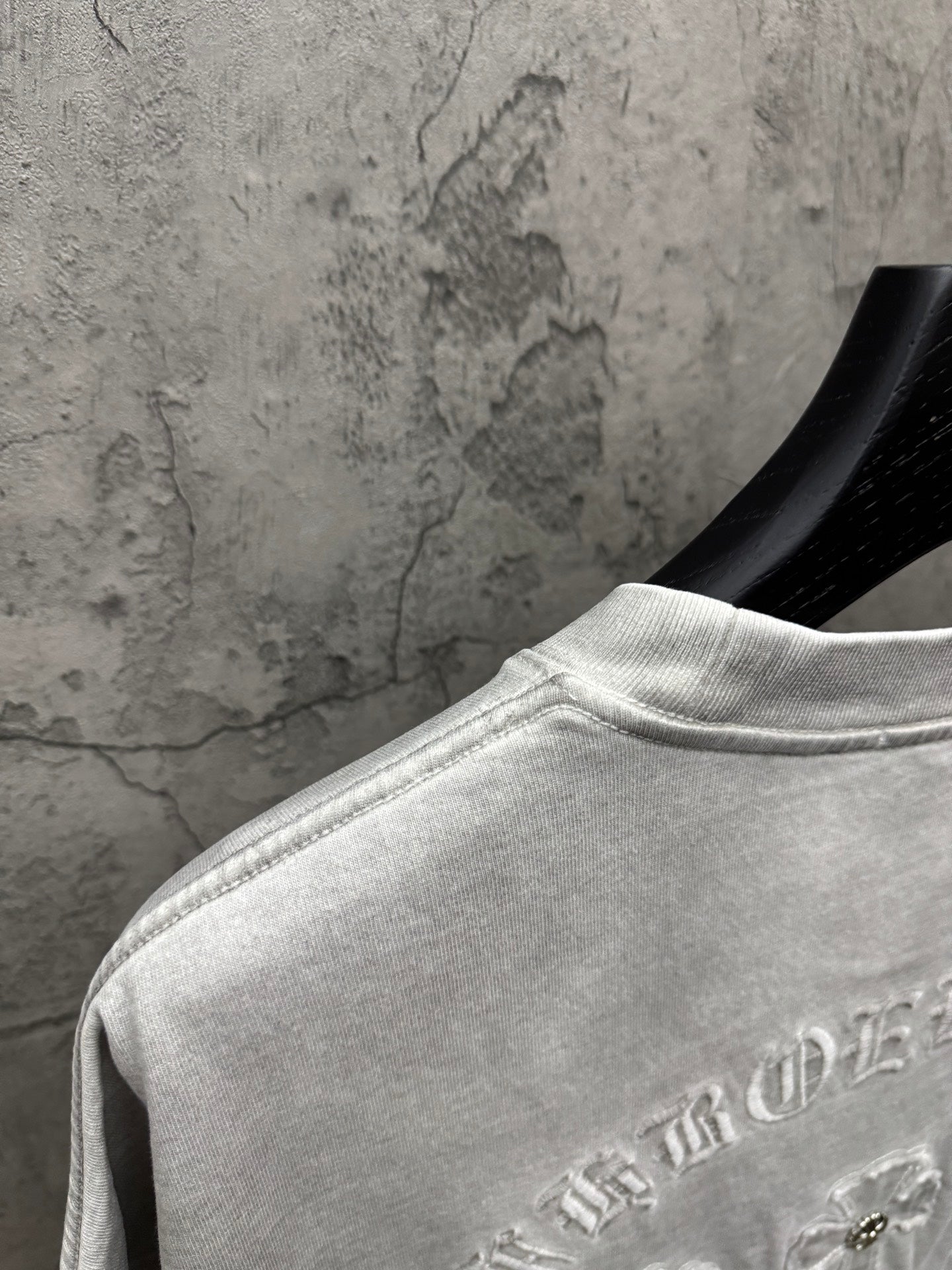 Light gray T-shirt back shoulder close-up with embroidered arched text near hem