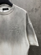 Light gray T-shirt front close-up with small circular chest embroidery and sleeve seam