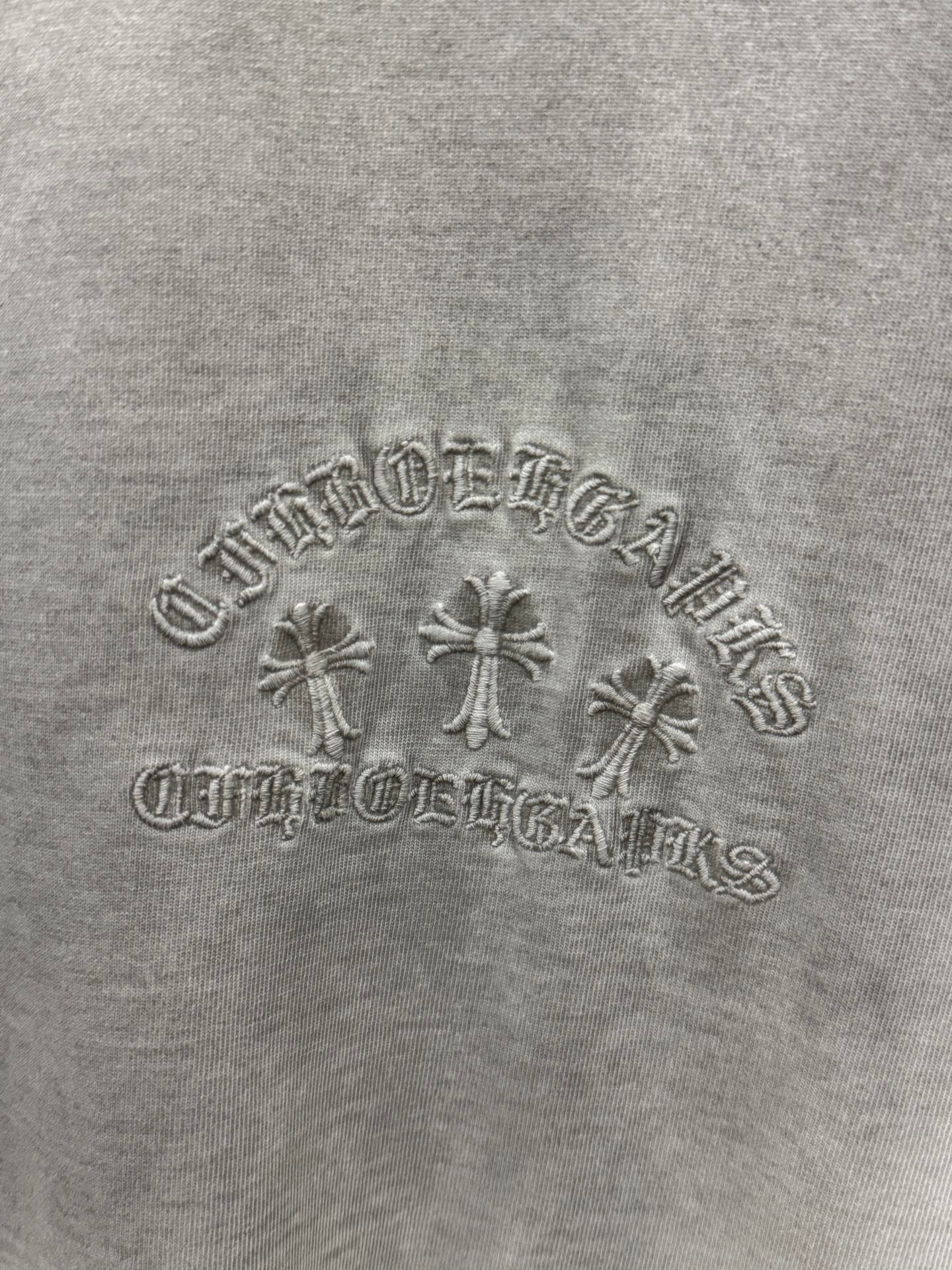 Light gray T-shirt chest embroidery close-up with floral cross and arched lettering