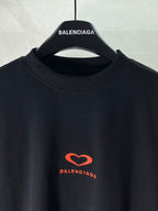 Black T-shirt close-up at crew neck with small red heart logo on chest
