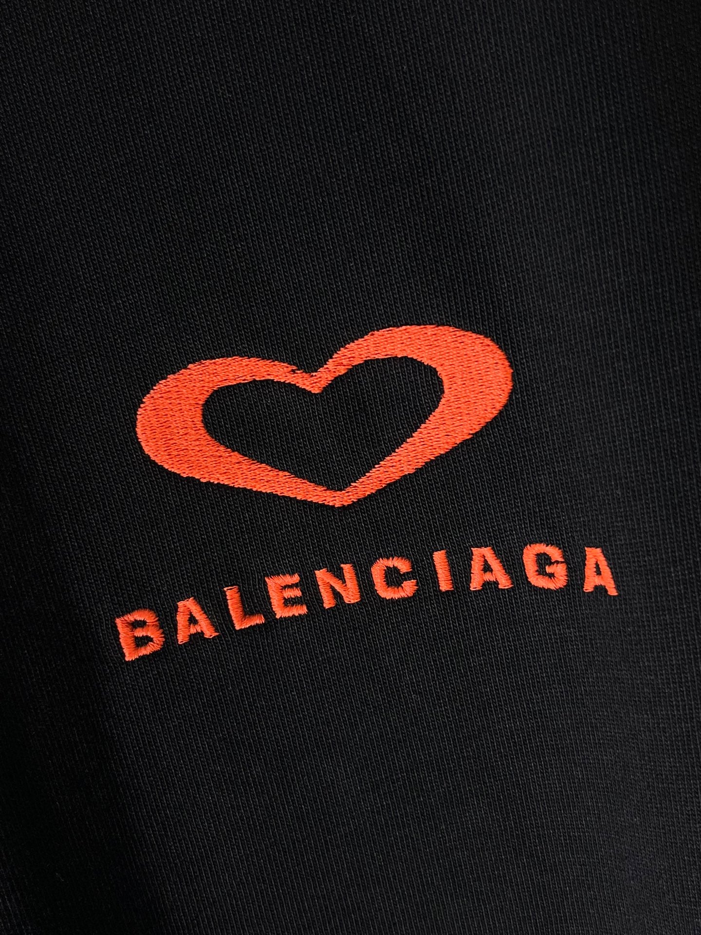 Black T-shirt fabric close-up with red heart emblem and Balenciaga text