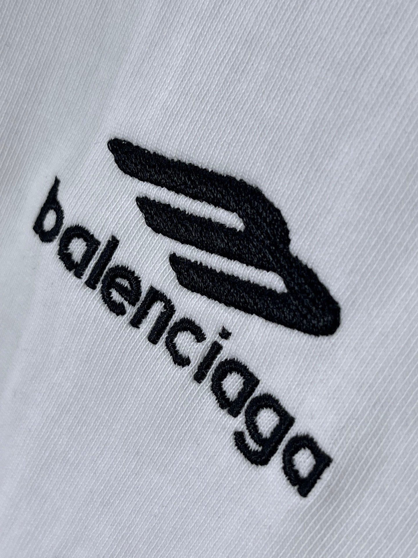 Balenciaga white T-shirt fabric close-up showing embroidered black logo