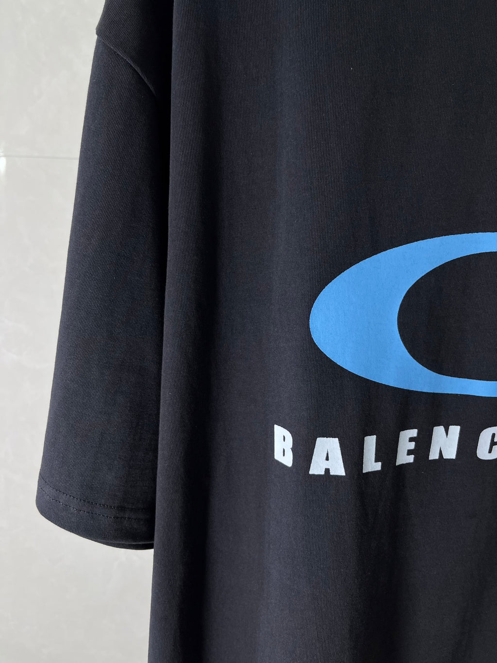 Balenciaga dark T-shirt sleeve/side with blue logo curve and partial BALENCIAGA