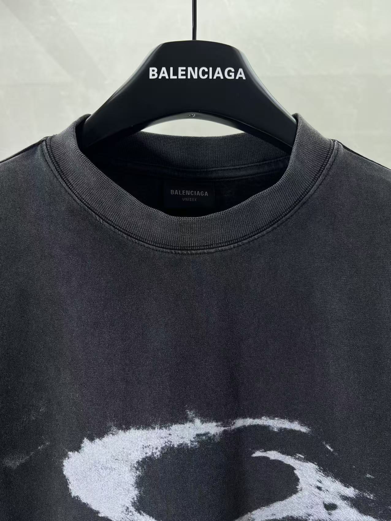 Balenciaga dark T-shirt neckline with “BALENCIAGA” logo on hanger; close-up