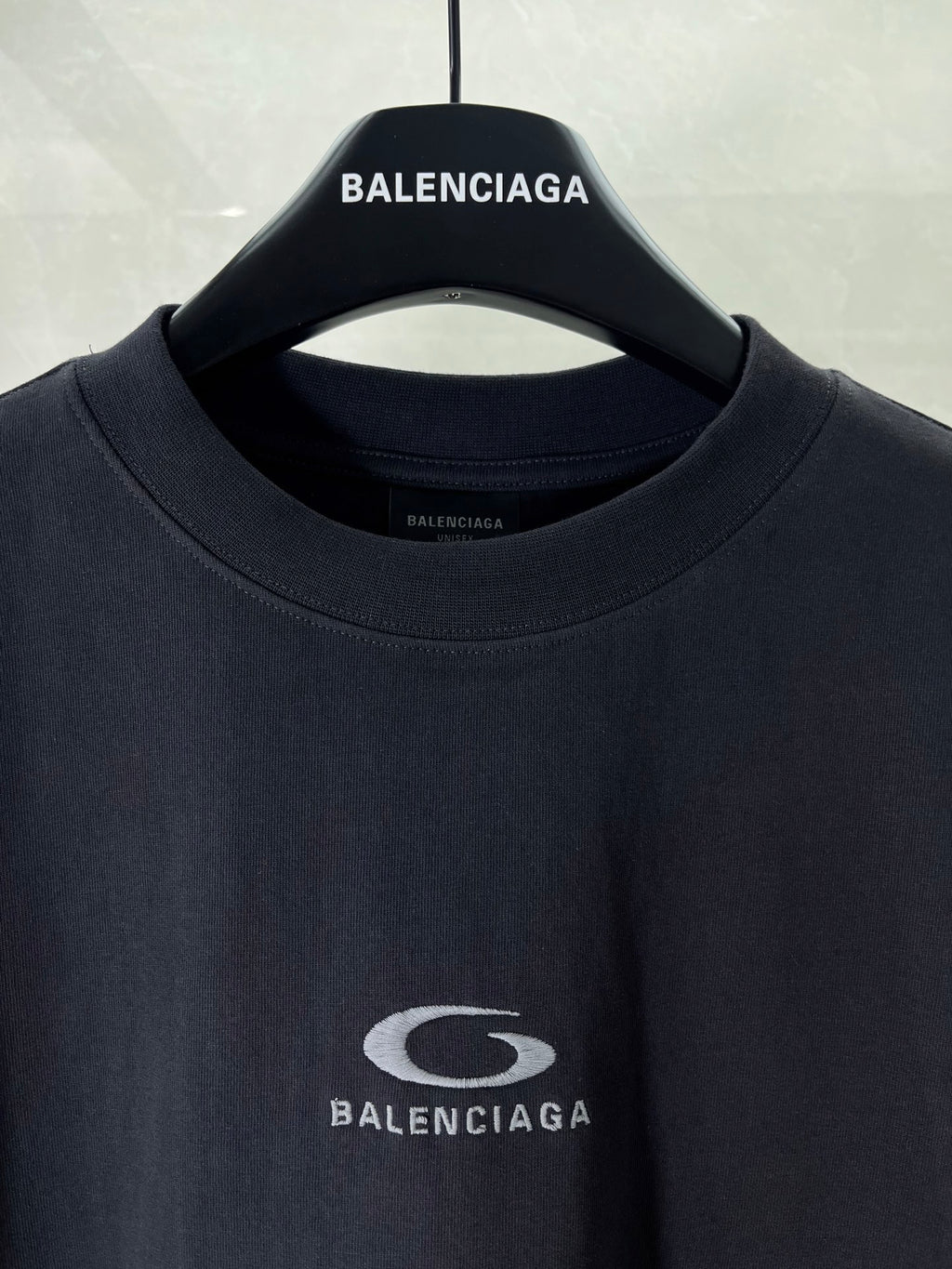 Dark T-shirt neckline with BALENCIAGA logo patch at center chest