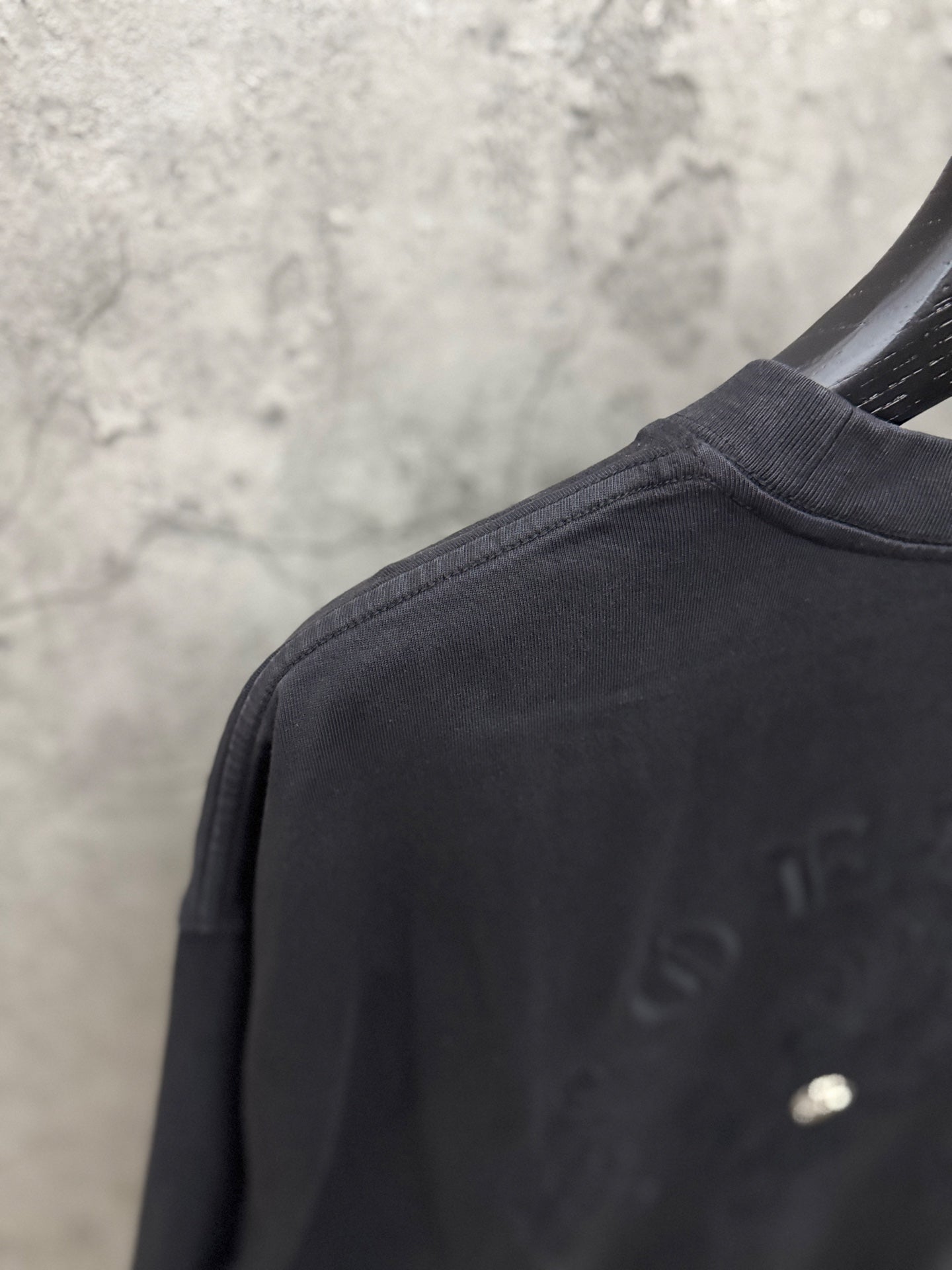 Black T-shirt crew neck and sleeve seam with small chest emblem detail.