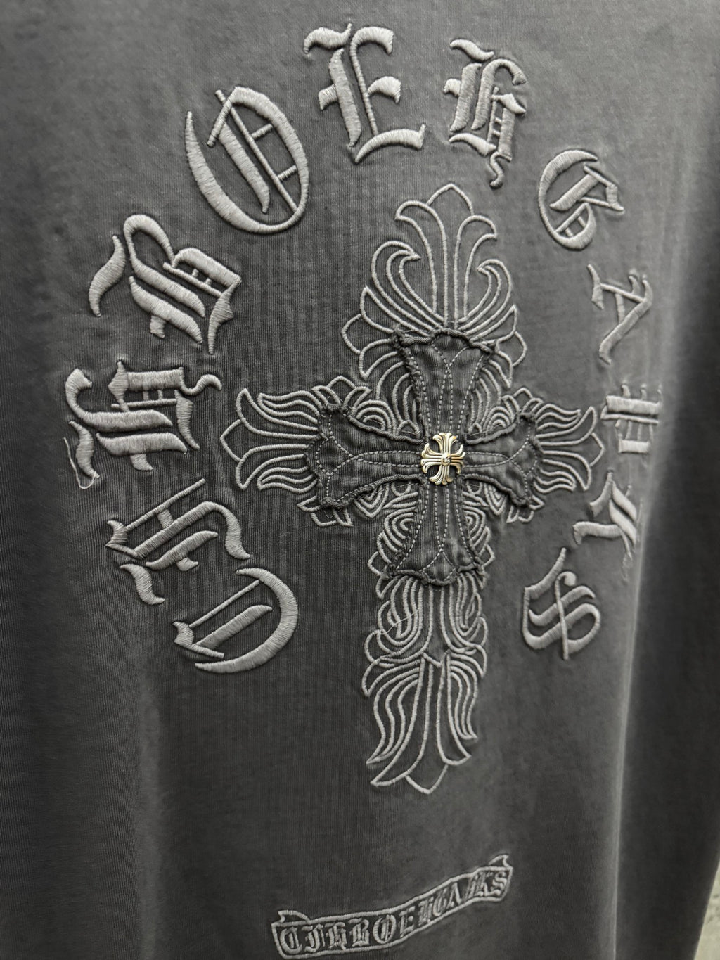 Dark gray T-shirt close-up of large cross emblem embroidery with gold accents