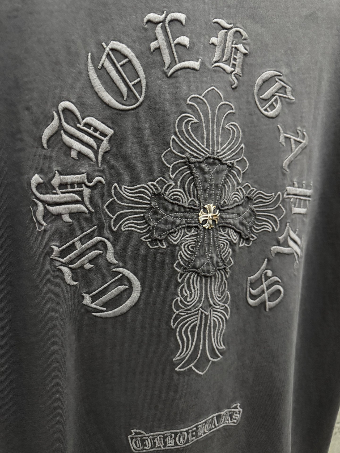 Dark gray T-shirt close-up of large cross emblem embroidery with gold accents