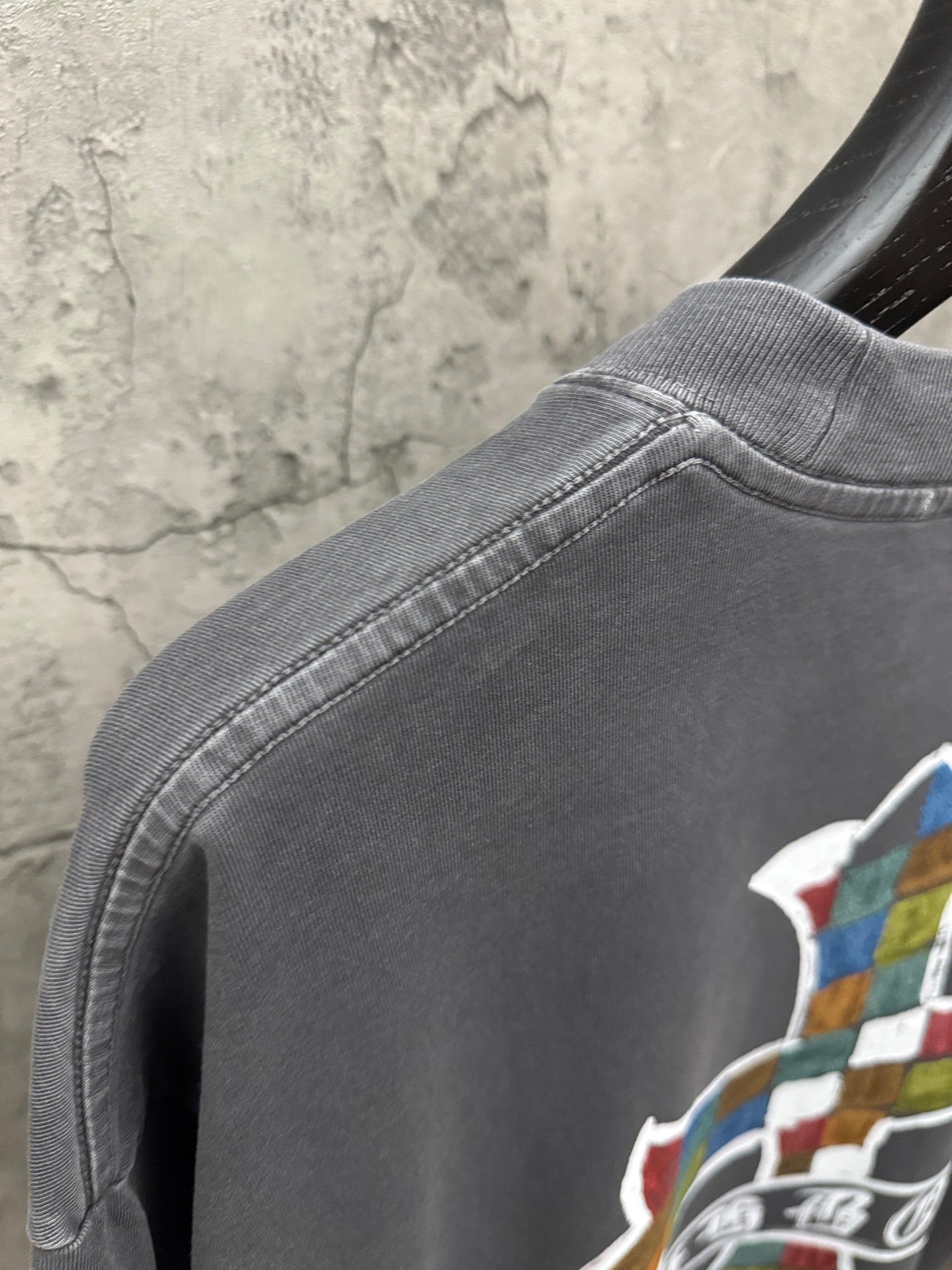 Dark gray T-shirt shoulder seam and neckline detail with partial cross graphic