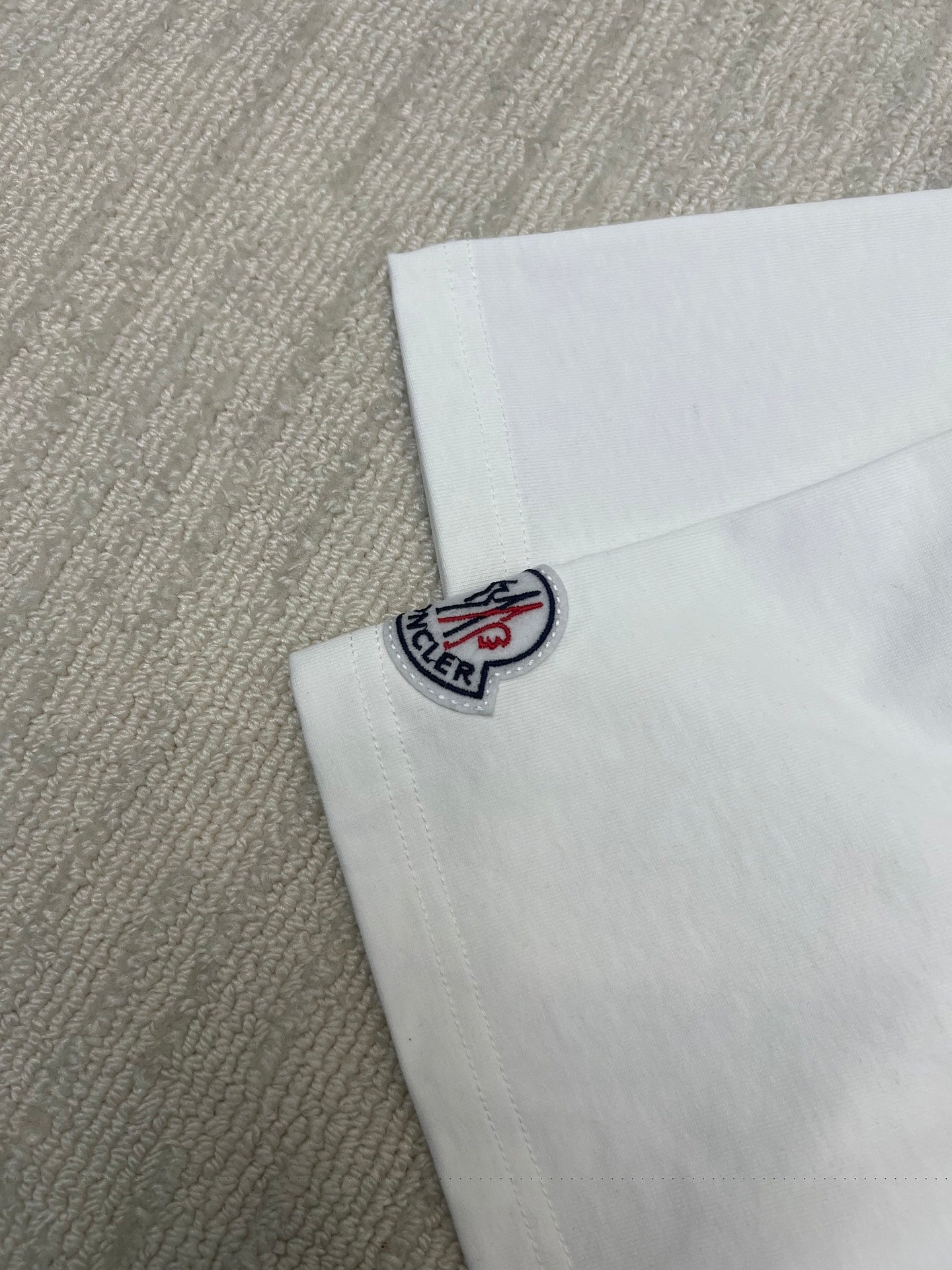 Close-up of Moncler logo patch on white T-shirt sleeve cuff