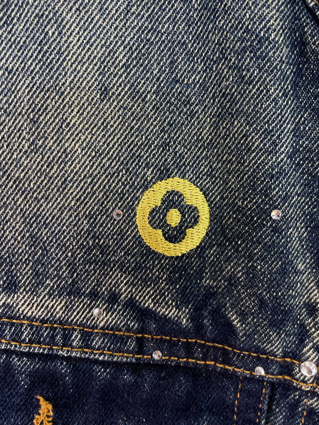 Denim jacket shoulder area with yellow circular emblem patch and silver studs