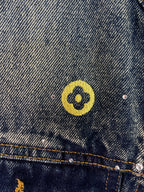 Denim jacket shoulder area with yellow circular emblem patch and silver studs
