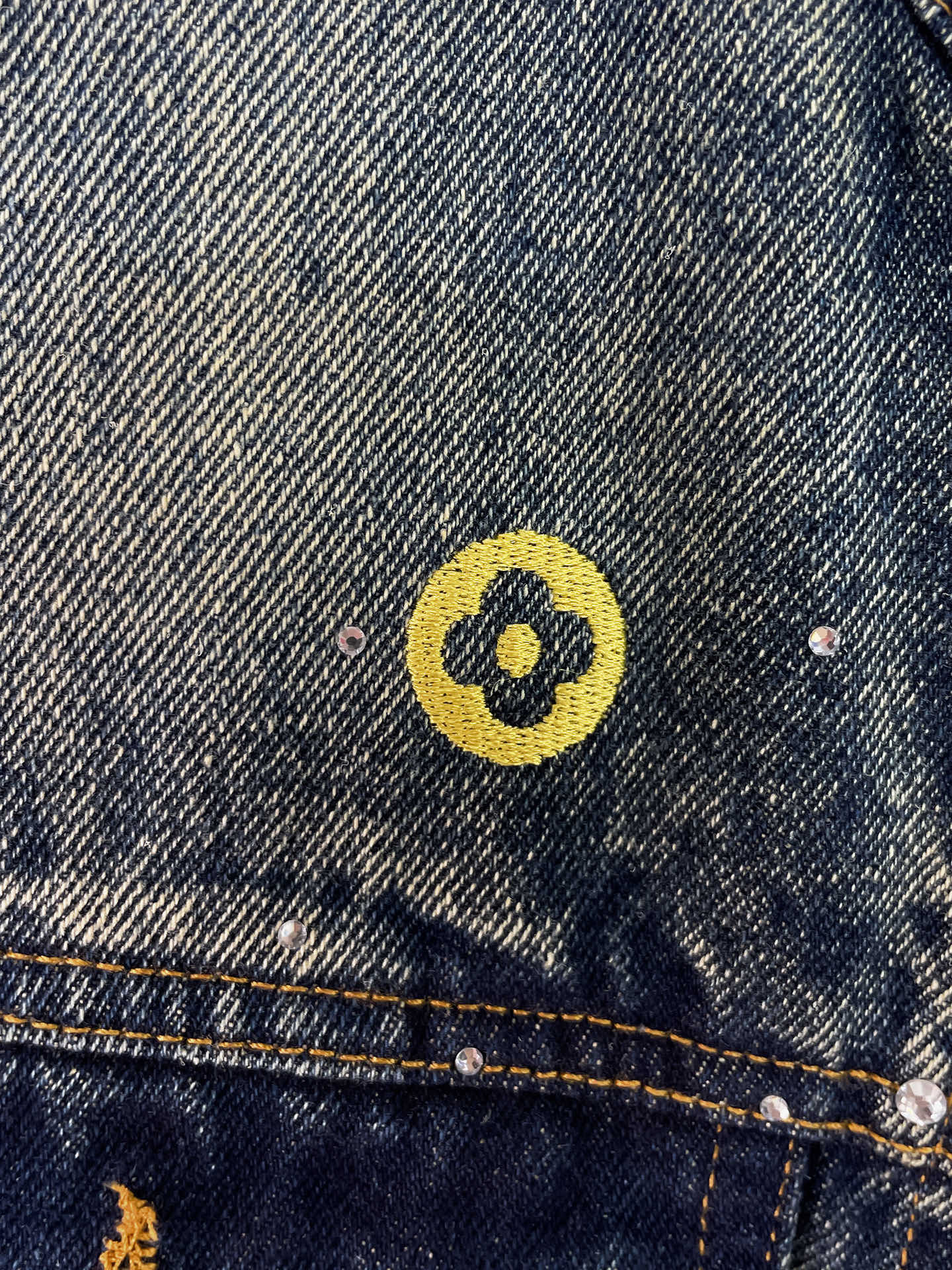 Denim jacket shoulder area with yellow circular emblem patch and silver studs