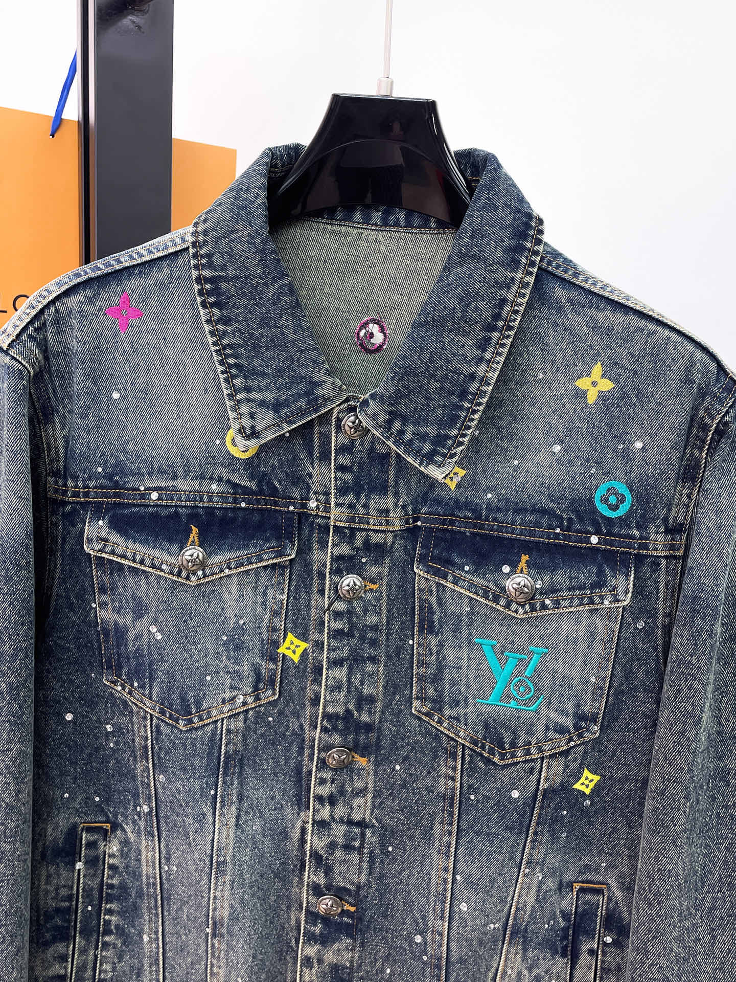 Denim jacket front with button chest pockets and colorful embroidered logo patches