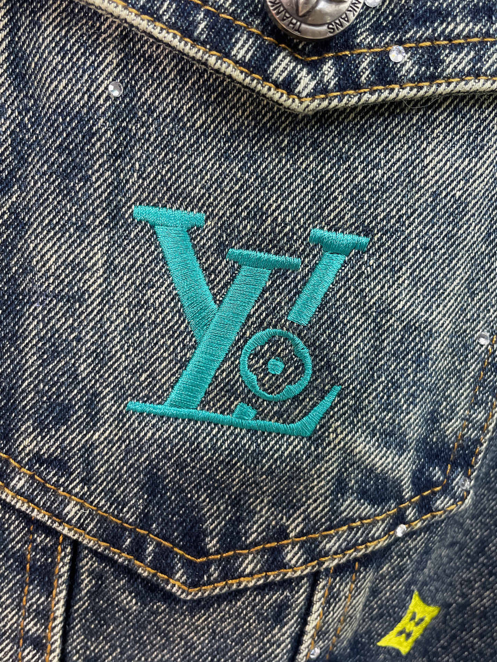 Denim jacket chest pocket with turquoise LV-style logo embroidery and studs