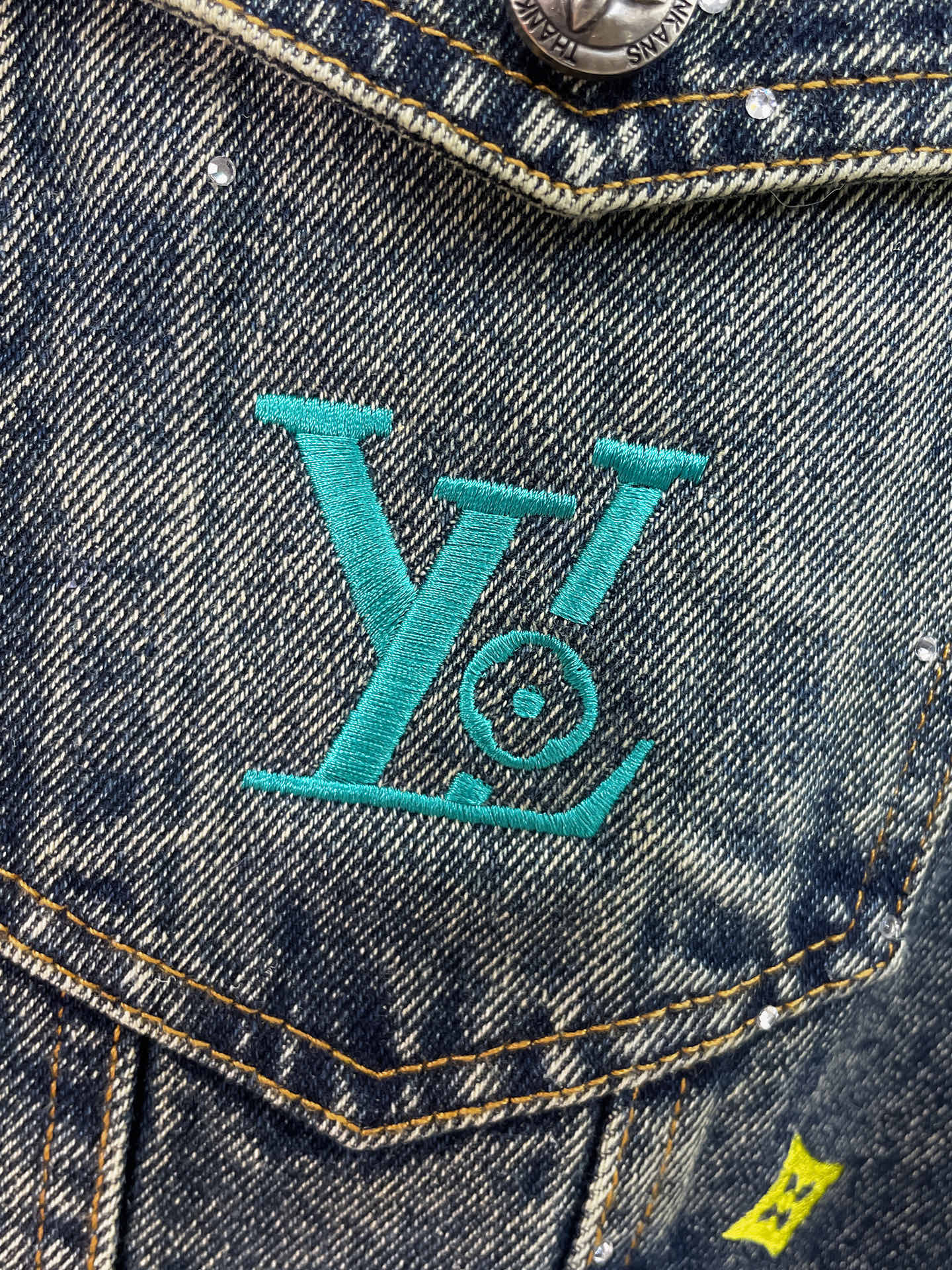 Denim jacket chest pocket with turquoise LV-style logo embroidery and studs