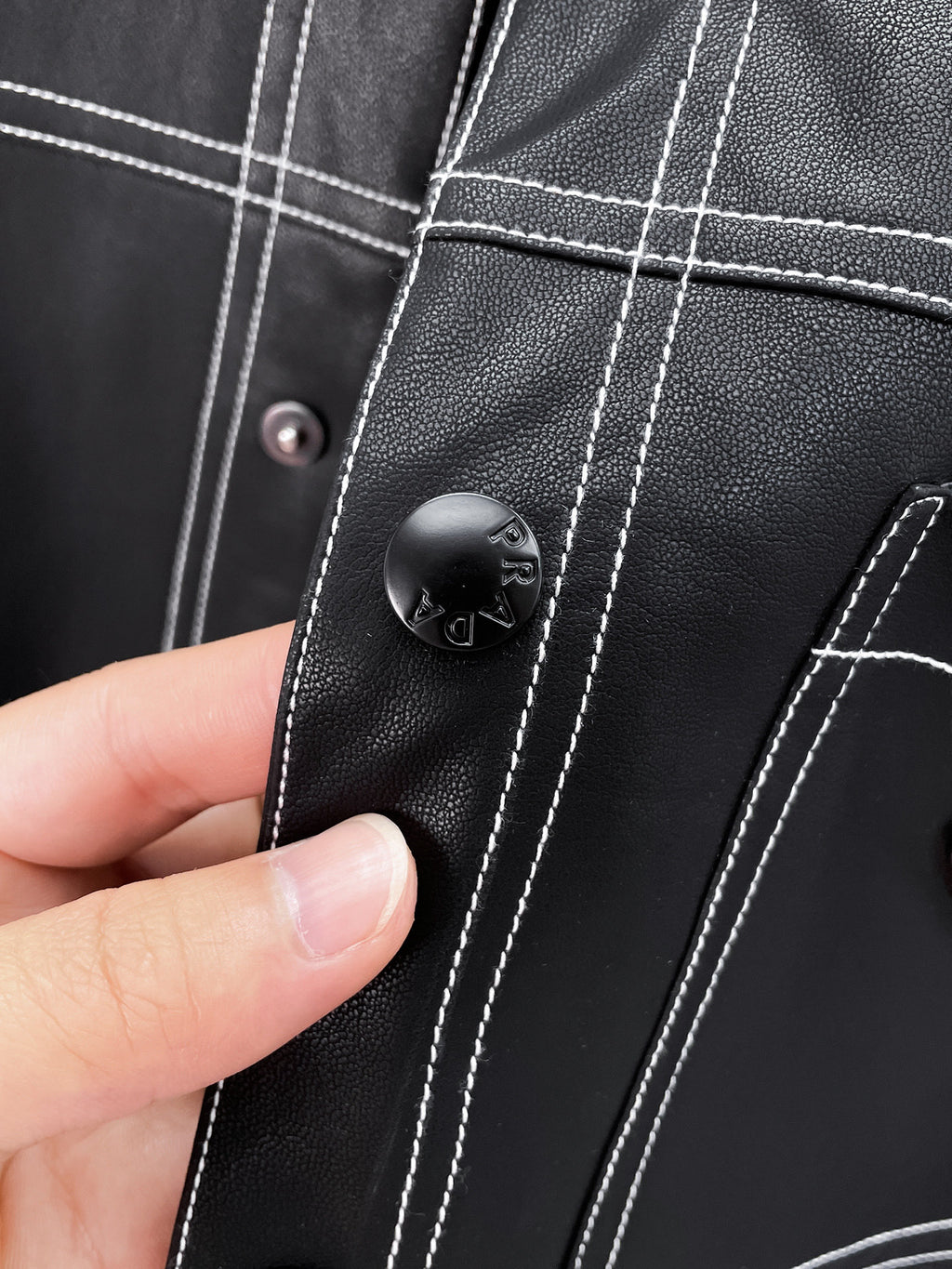 Black leather jacket detail with Prada button and contrast stitching