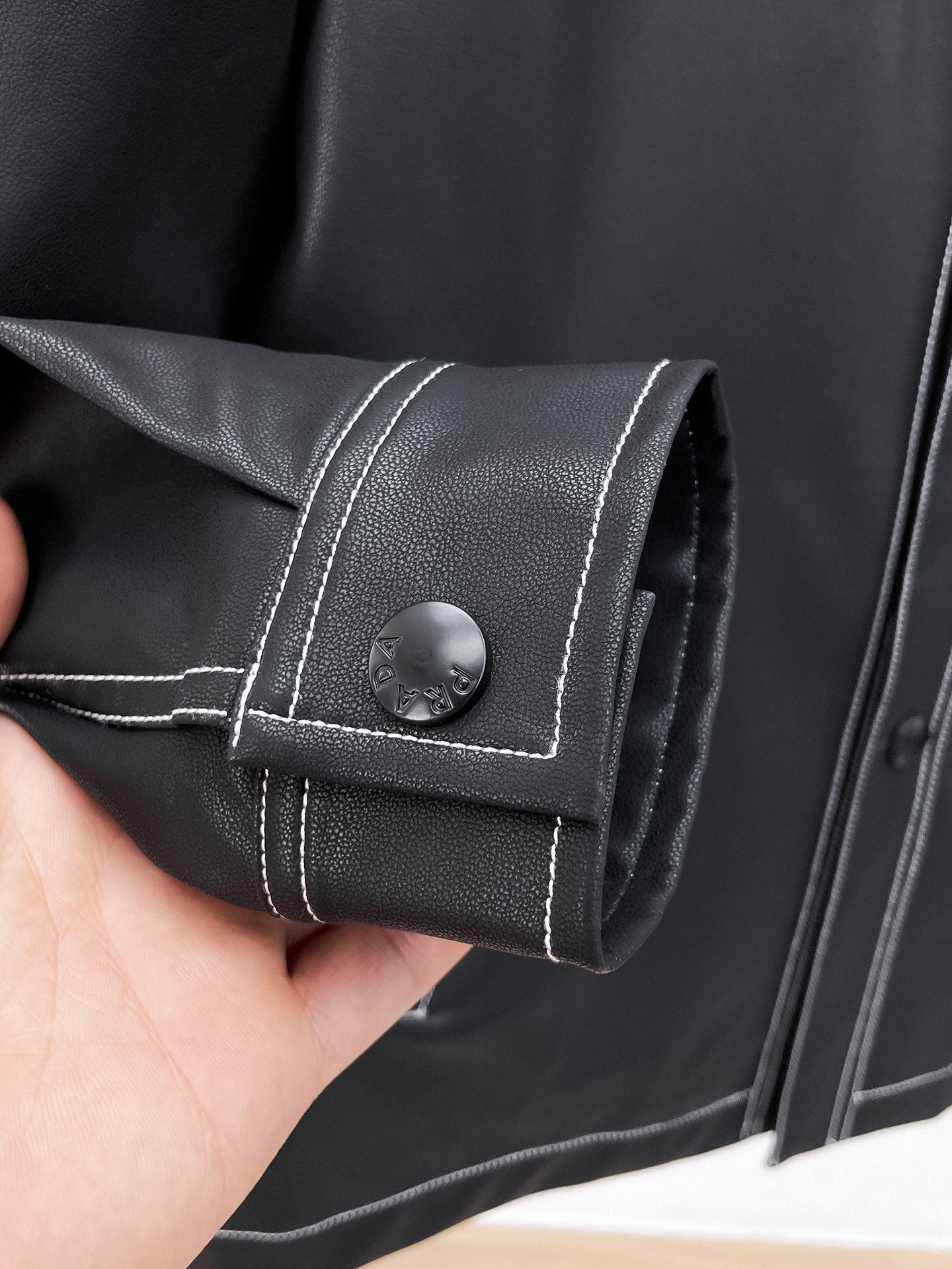 Black leather jacket cuff with contrast stitching and snap button