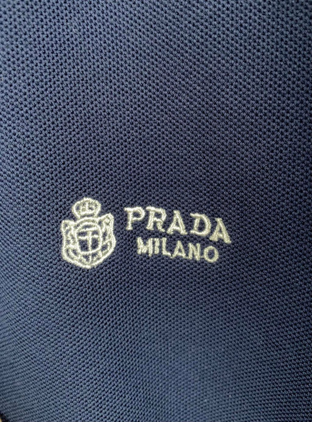 Close-up of Prada Milano logo on navy knit polo fabric