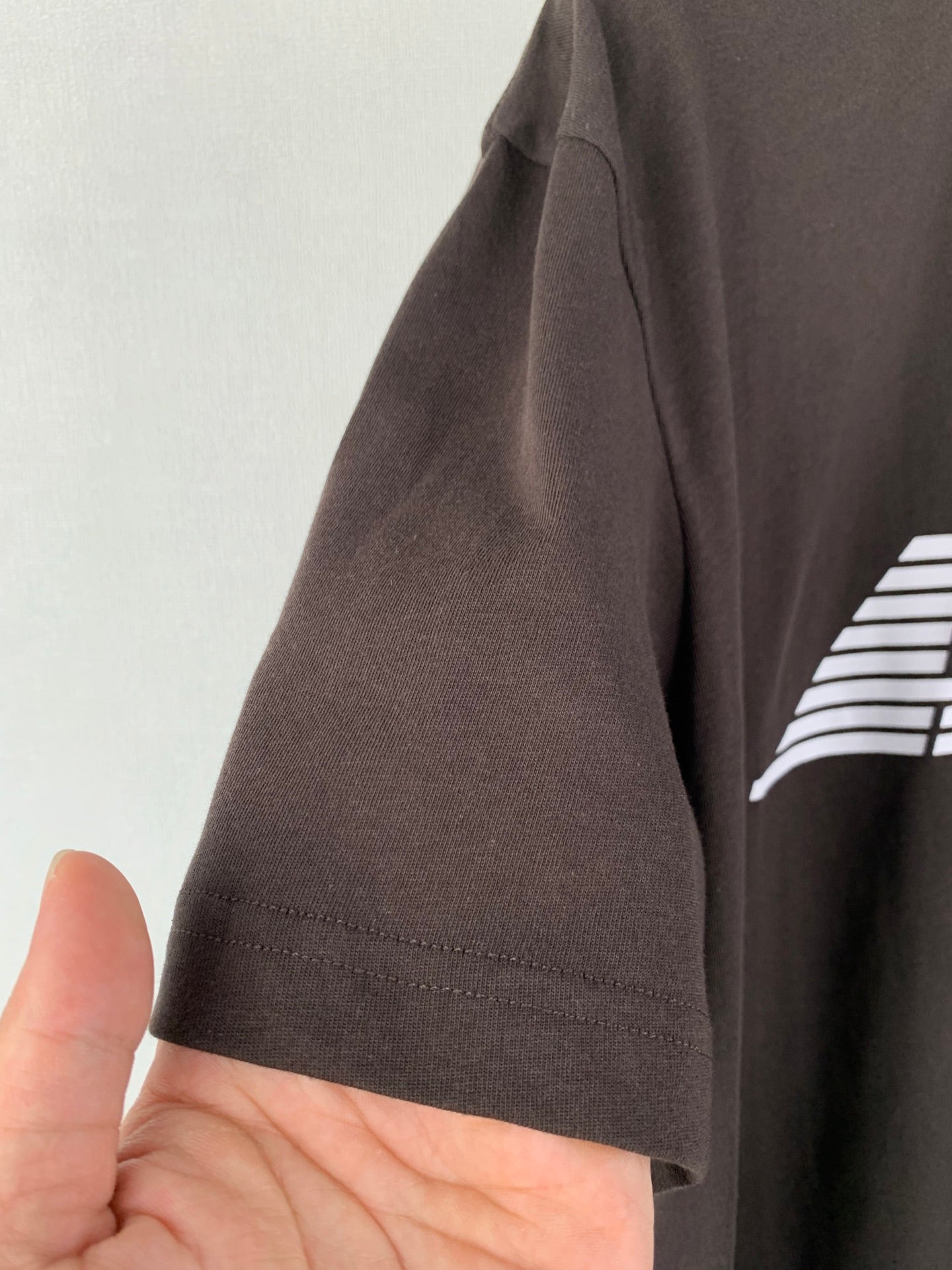 Side view of dark brown T-shirt sleeve with stitched hem and small front graphic