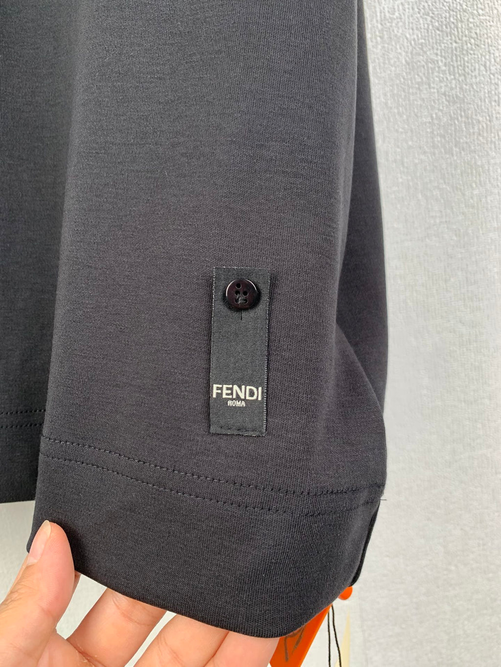 Dark T-shirt sleeve hem with FENDI label and small buttoned tab