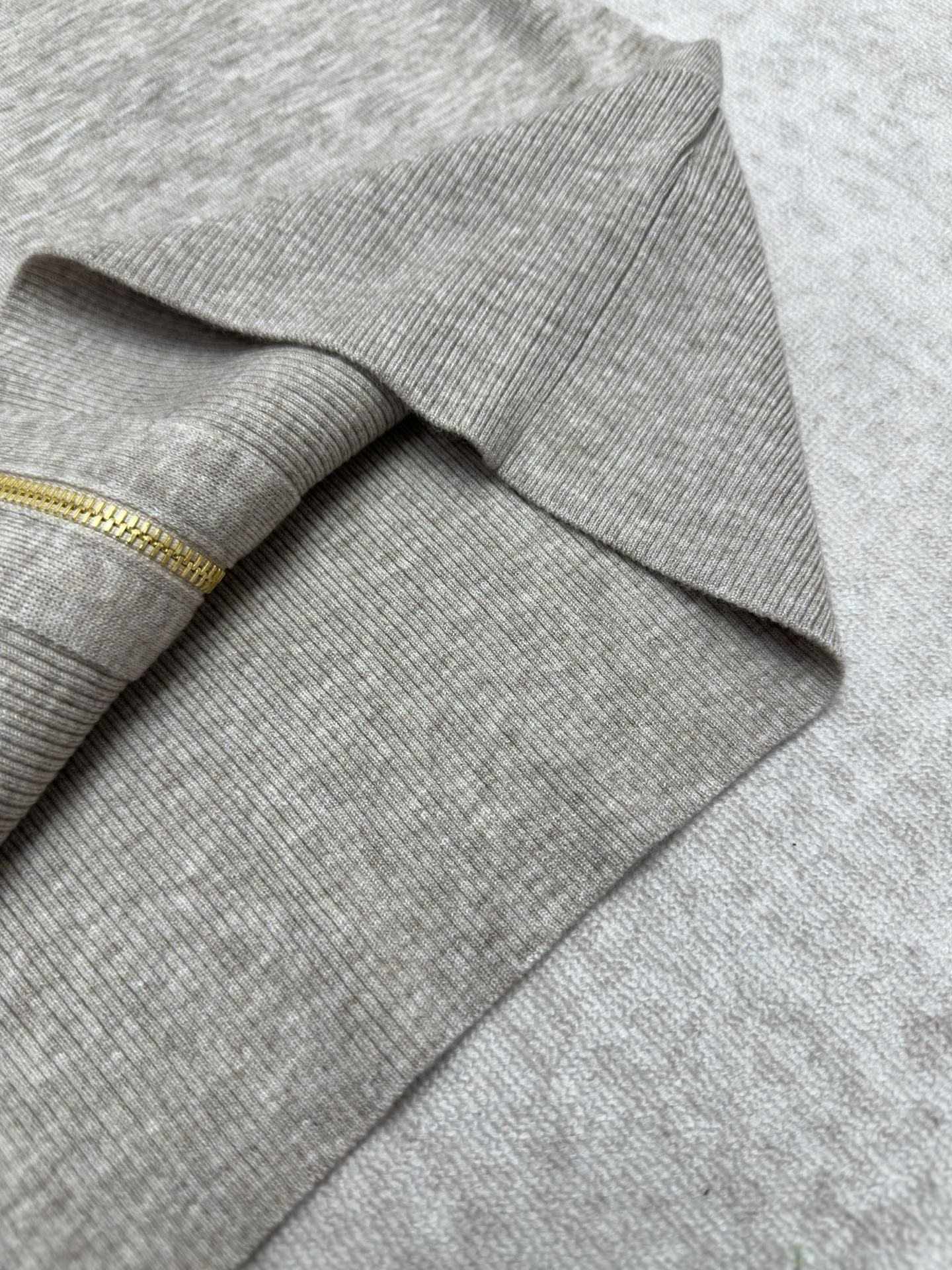 Ribbed cuff and sleeve end on heather gray sweater with gold zipper trim