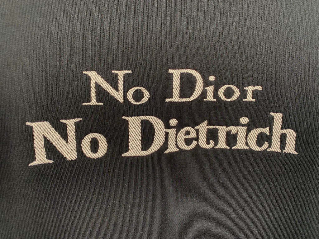 Close-up of gold “No Dior No Dietrich” print on black sweatshirt