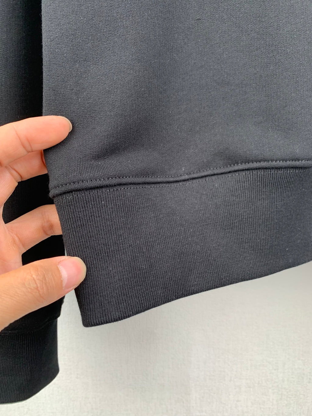 Close-up of black sweatshirt hem with curved seam and ribbed cuff