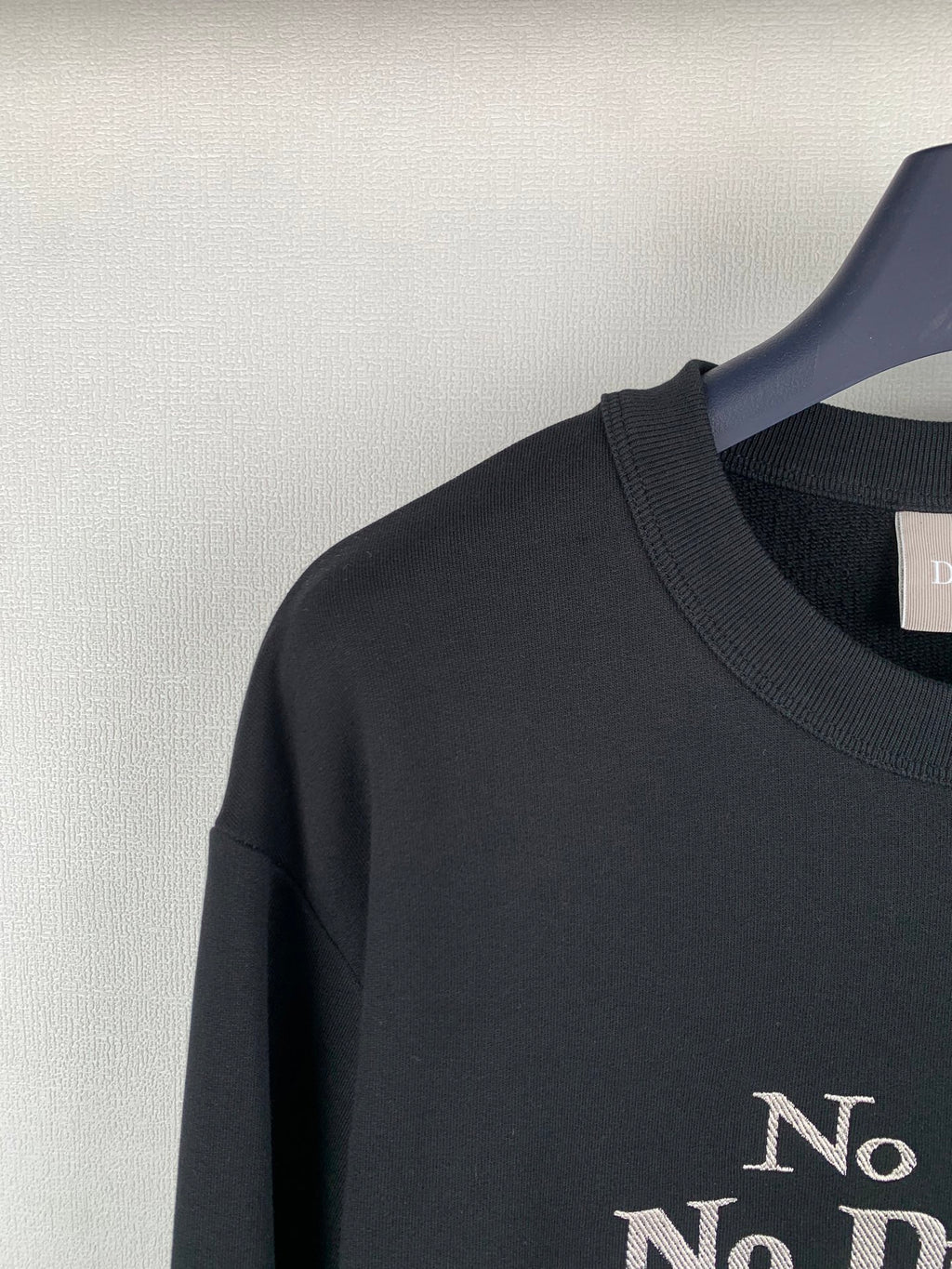Black crewneck sweatshirt shoulder with partial “No” gold print
