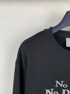 Black crewneck sweatshirt shoulder with partial “No” gold print