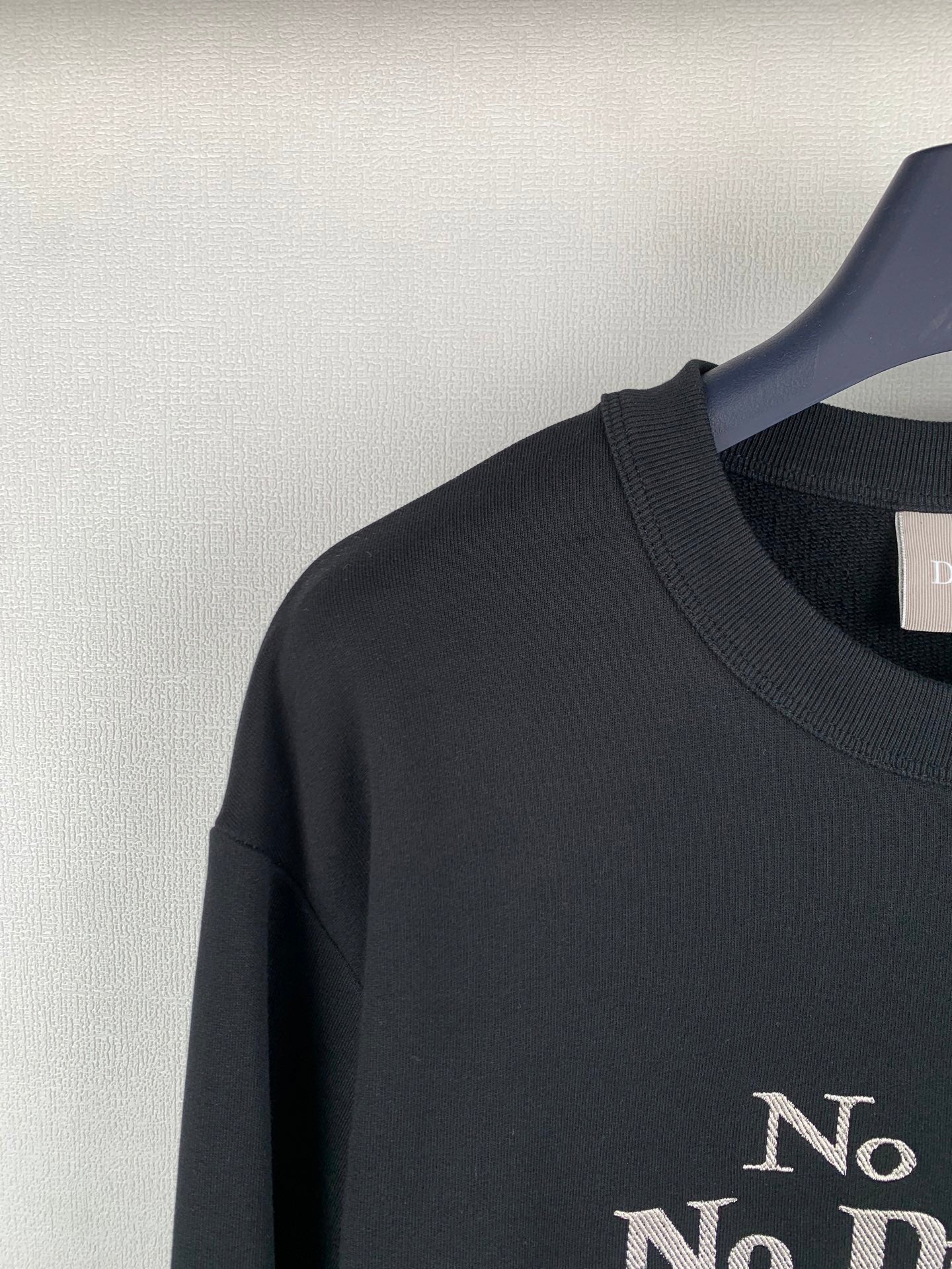Black crewneck sweatshirt shoulder with partial “No” gold print