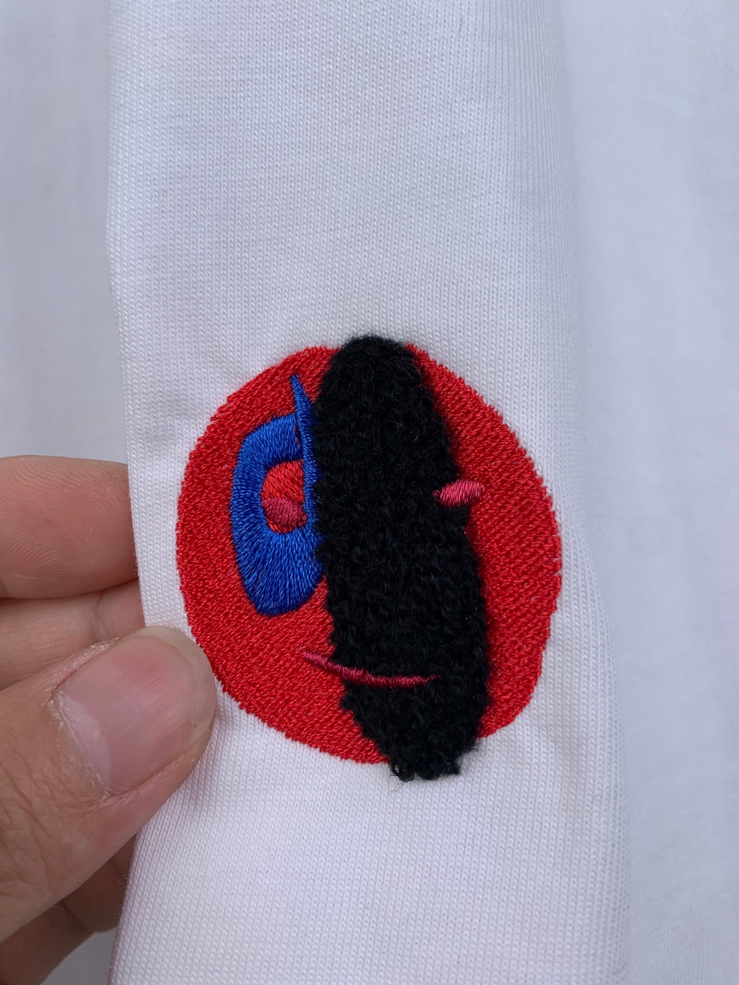 Off white T-shirt with embroidered red circular logo and black-blue figure