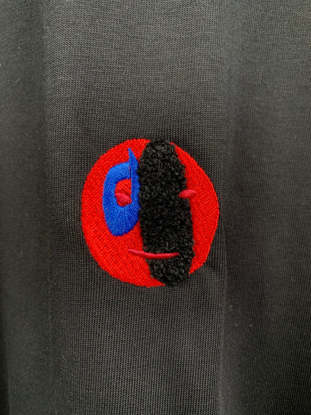 Close-up chest logo on dark charcoal crewneck T-shirt with red and blue graphic