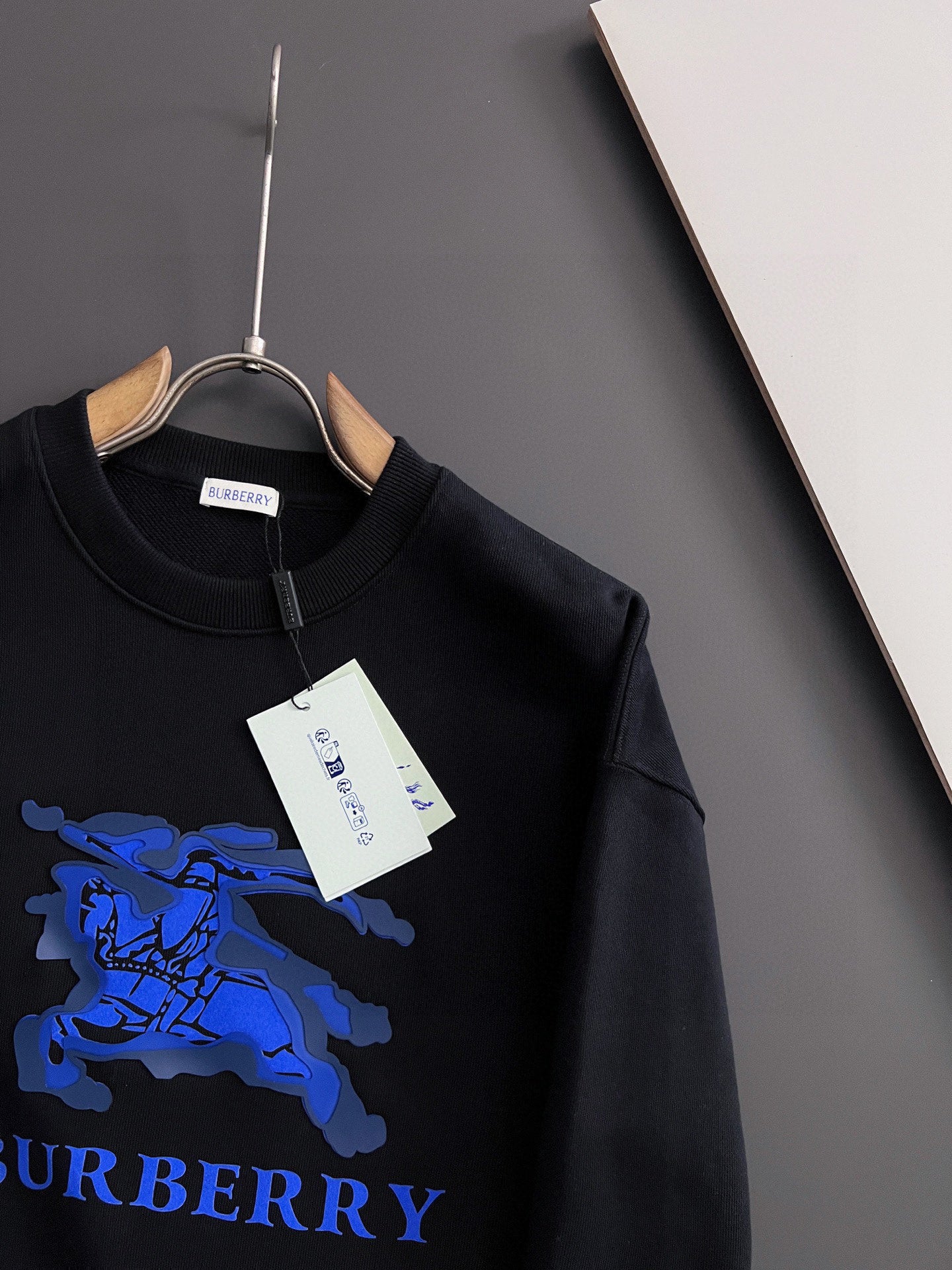 Black sweatshirt with blue horse graphic detail and white hang tag at top.