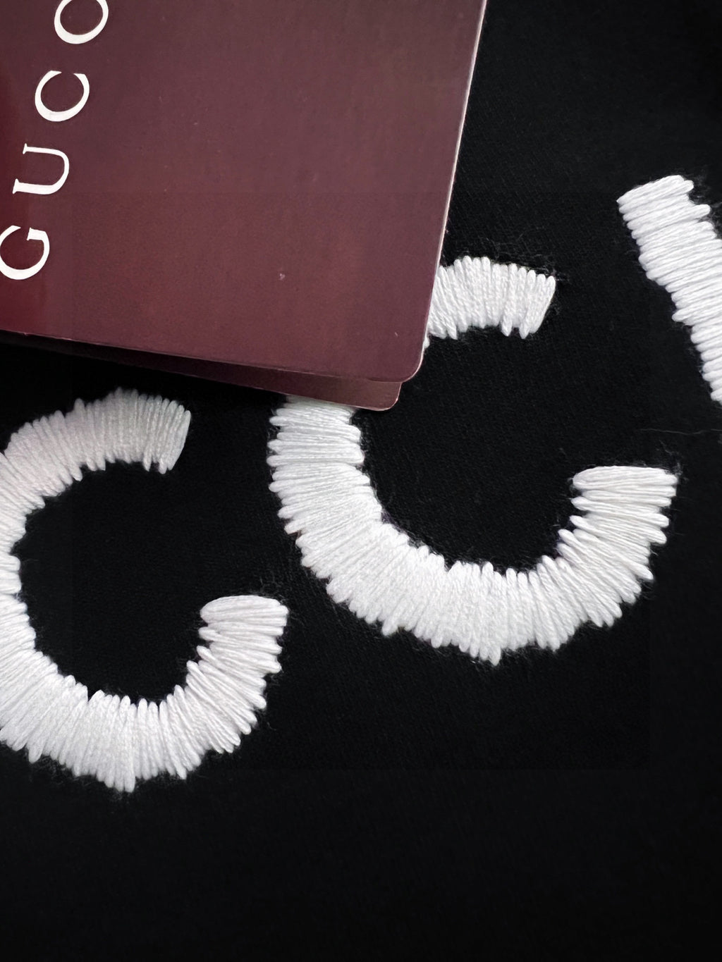 Black Gucci sweatshirt fabric with large white embroidered “GU” letters