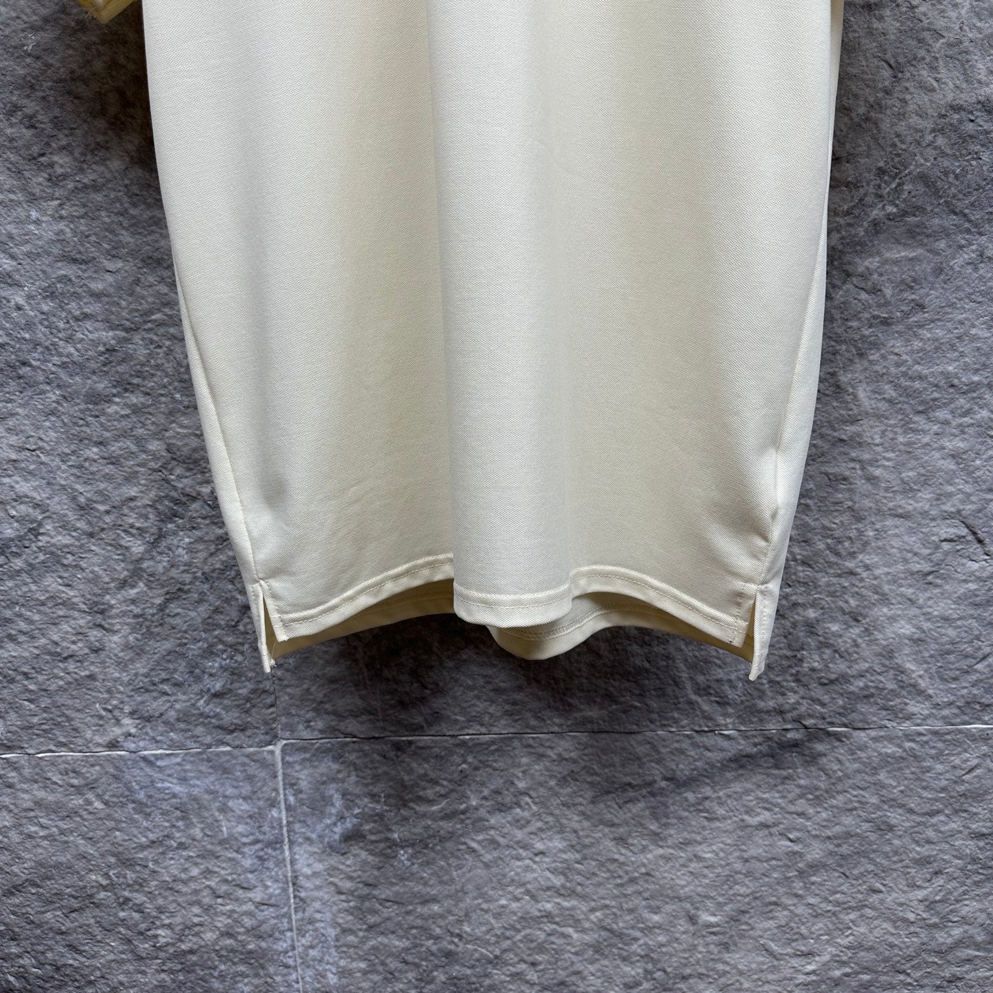 Cream polo shirt with curved hem and side vent, hanging