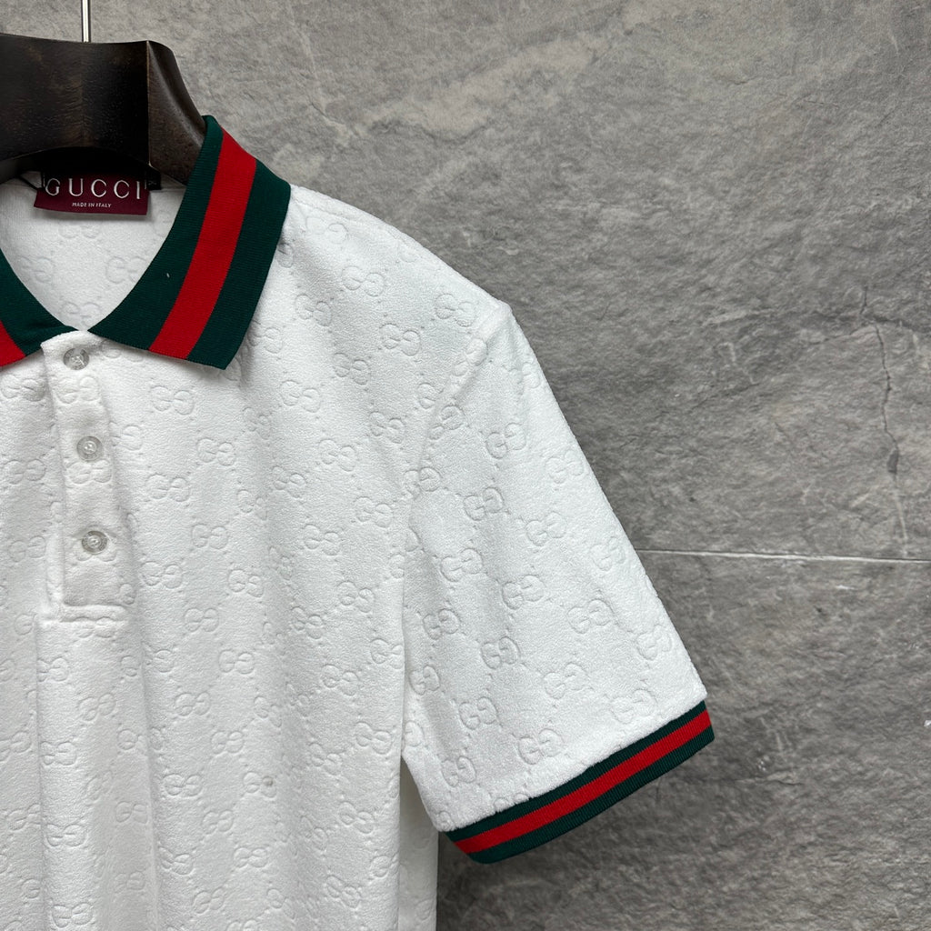 Gucci white polo shirt with embossed GG pattern and green-red striped sleeve edge.