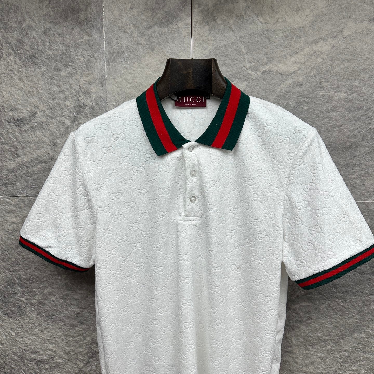 Gucci white polo shirt with embossed GG pattern and green-red striped collar.