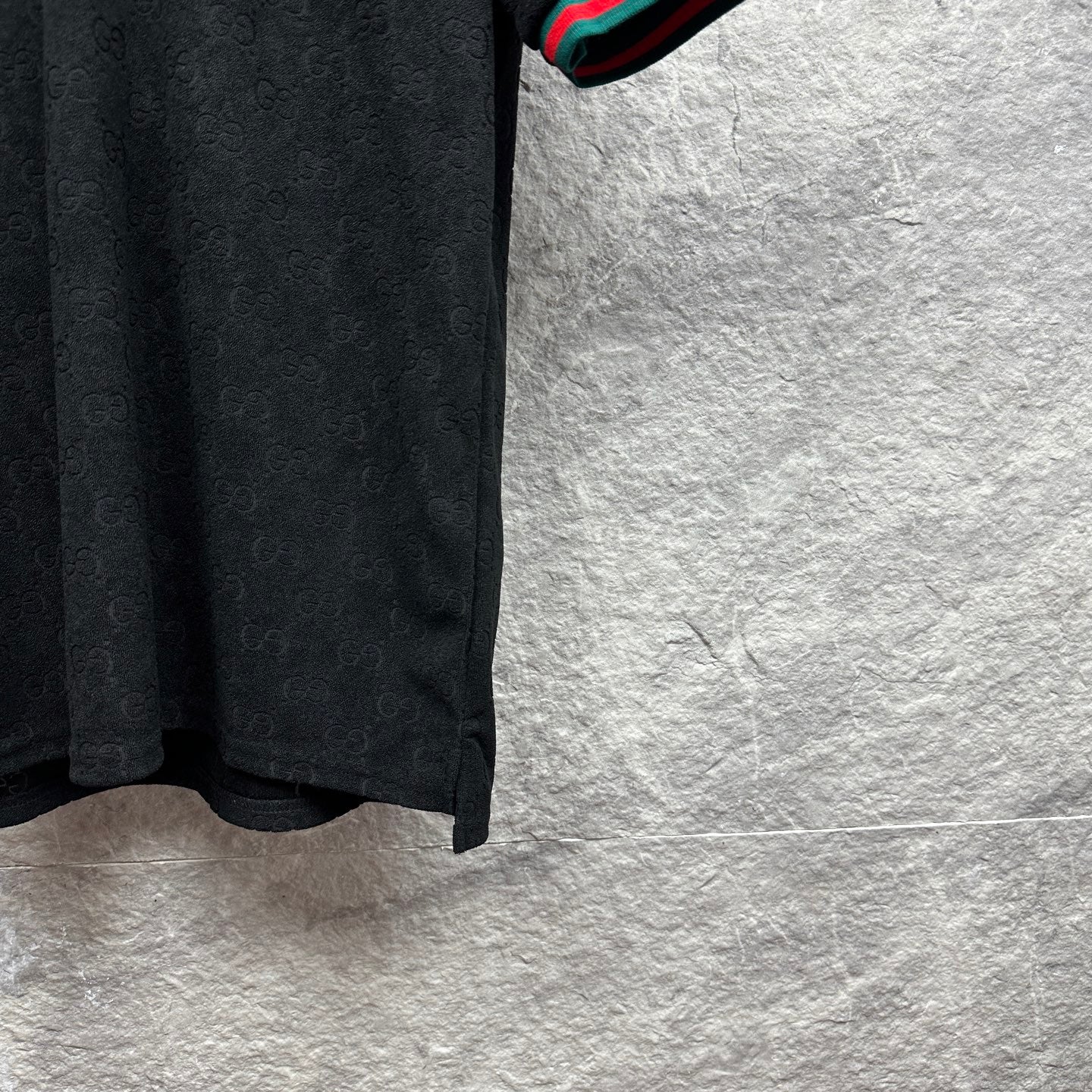 Gucci dark polo shirt side view with monogram pattern and striped cuff edge