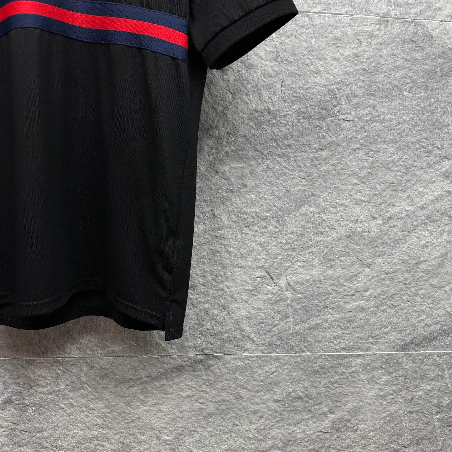 Black Gucci polo shirt side hem with blue-red striped band at chest.