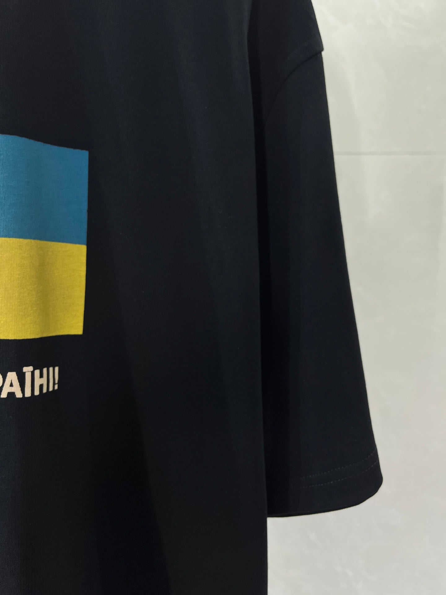 Balenciaga T-shirt sleeve and hem detail with blue-yellow flag graphic and partial text