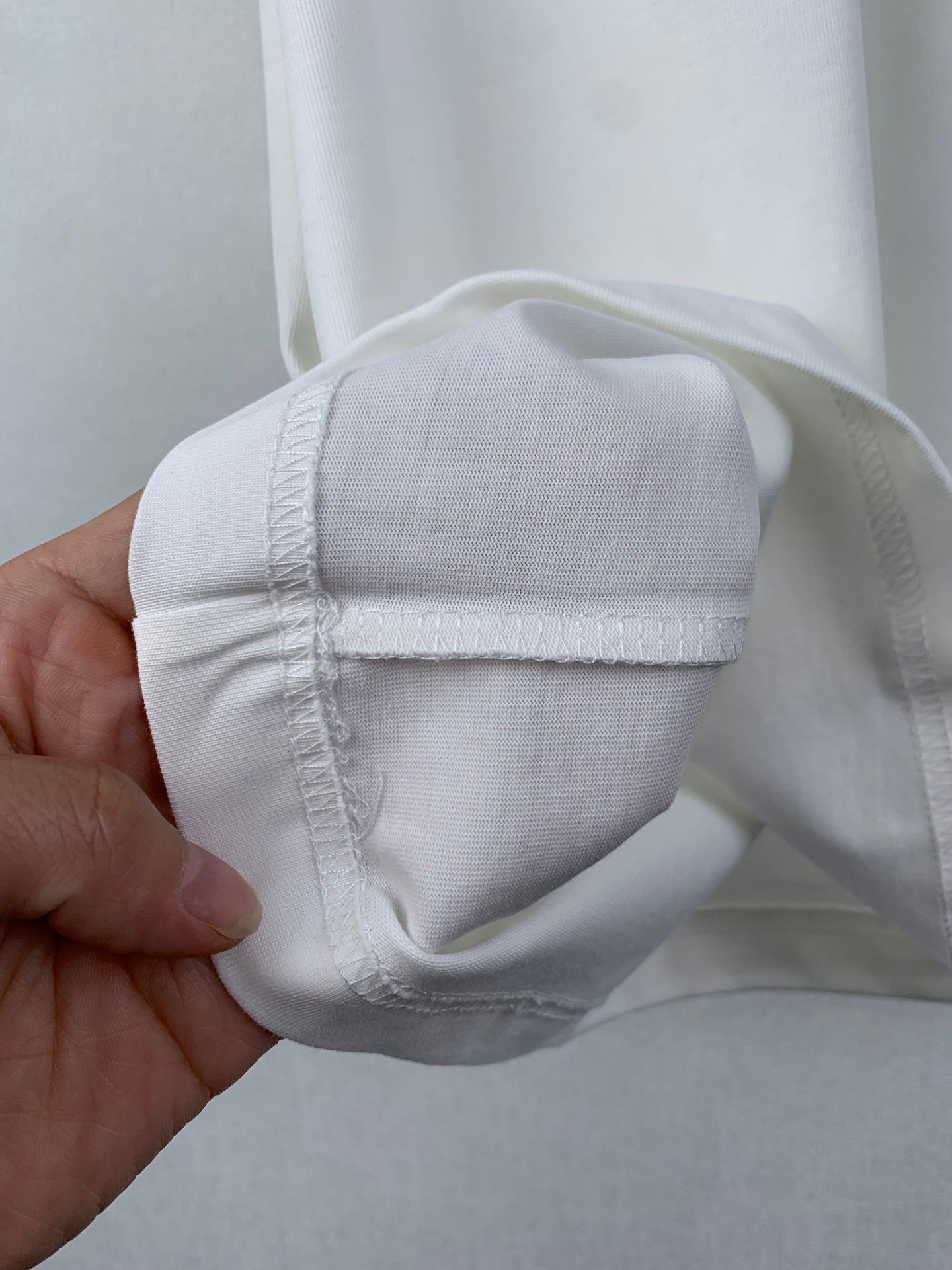 White T-shirt cuff with reinforced stitching, folded and held in hand.
