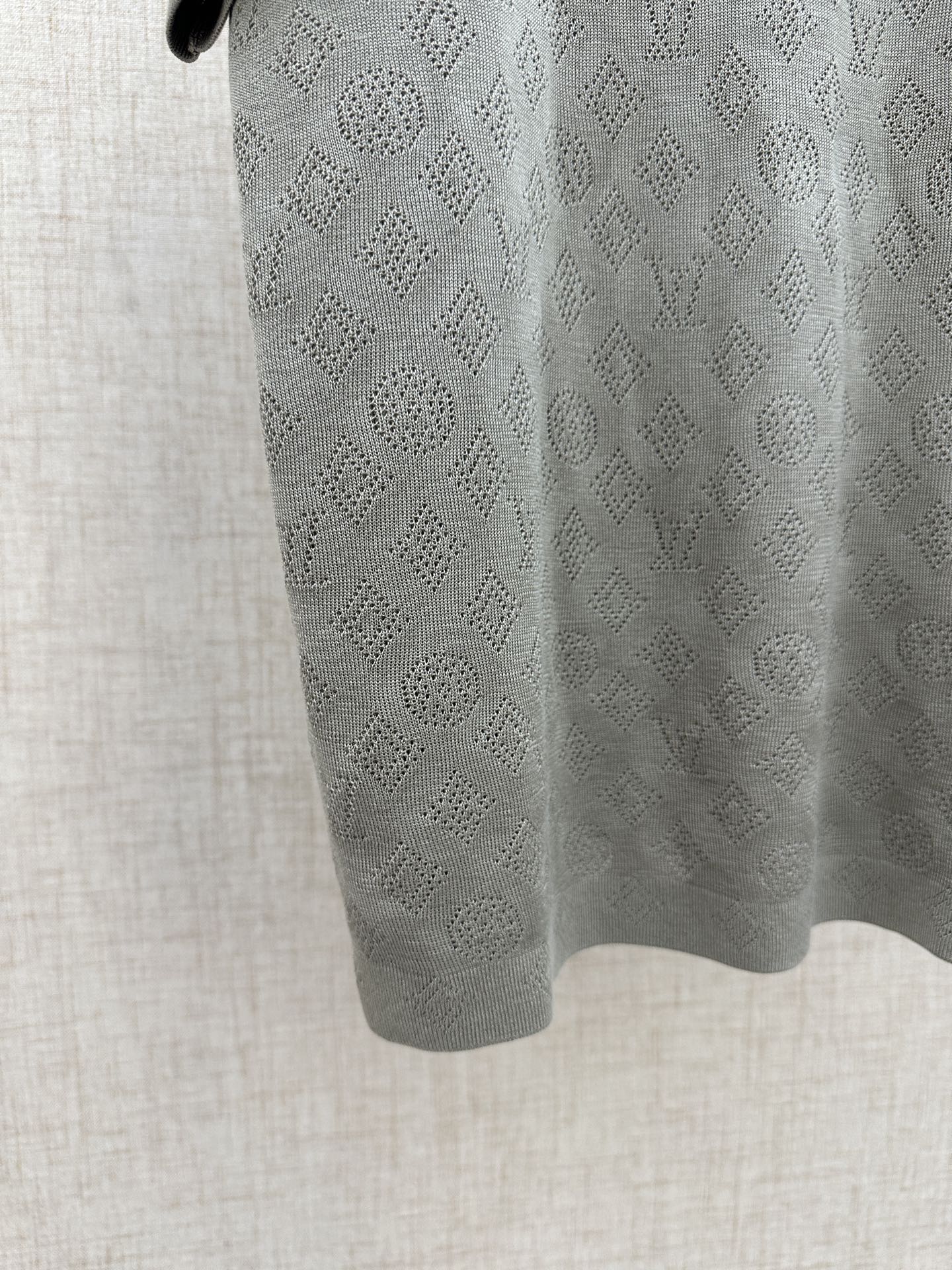 Light gray polo shirt fabric close-up with repeating monogram pattern