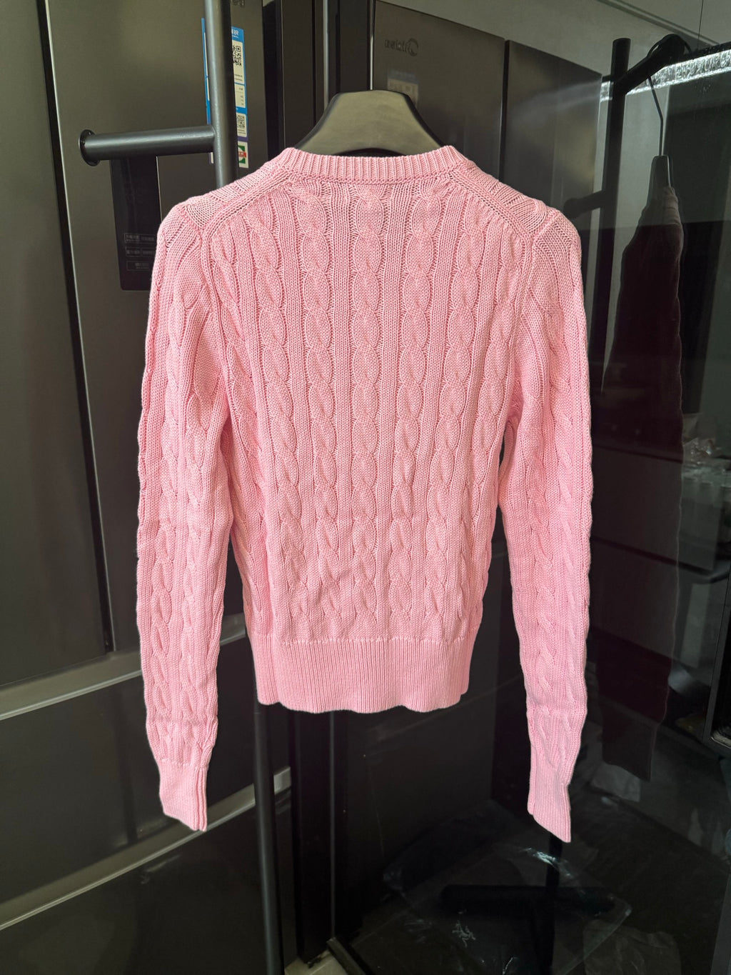 Pink cable-knit cardigan sweater, back view with ribbed hem and long sleeves.