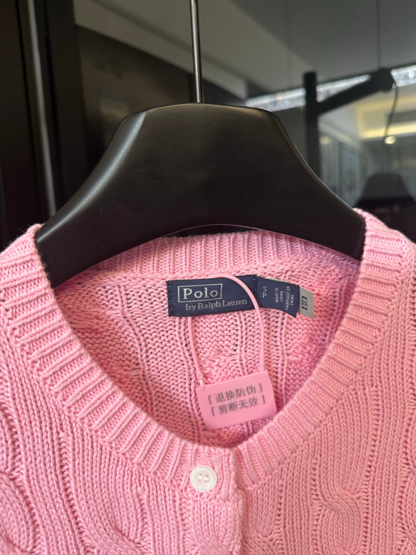 Pink cable-knit cardigan on hanger with Polo by Ralph Lauren neck label and buttons.
